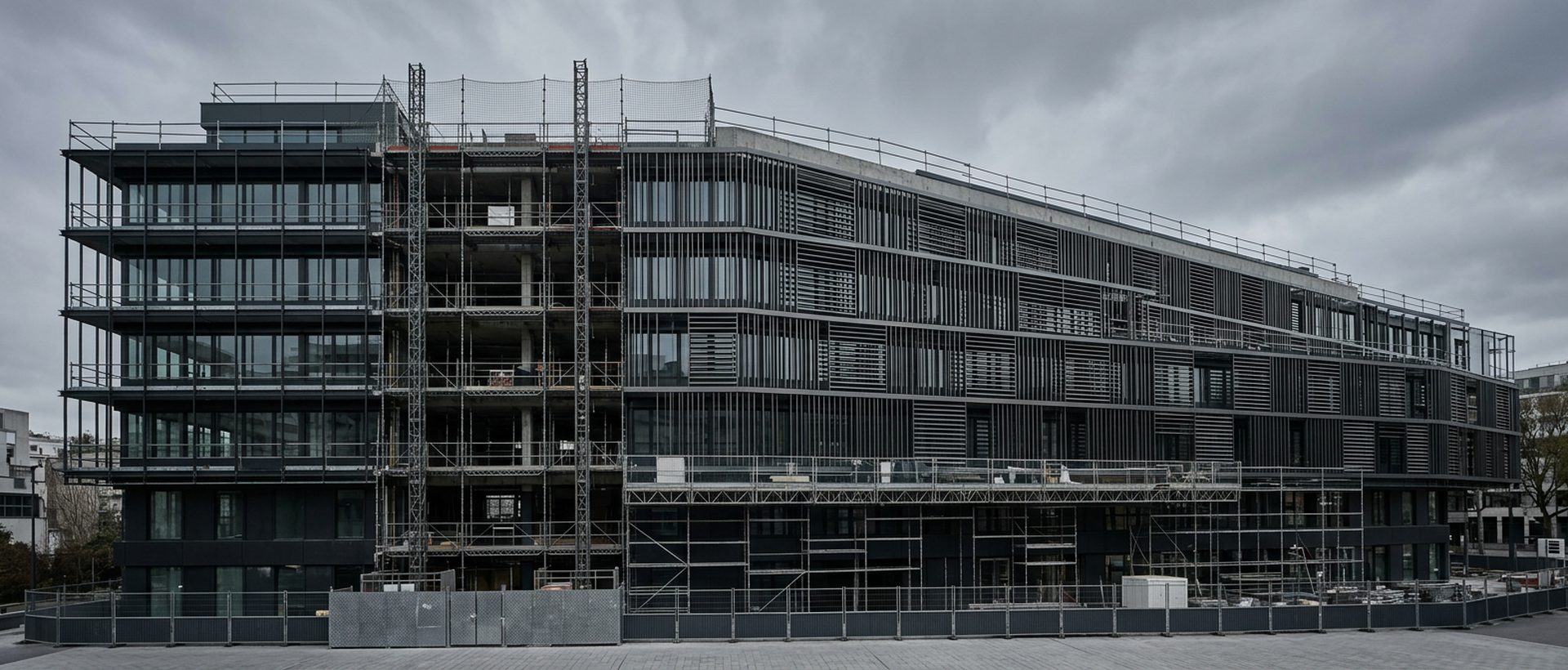 Façade d'immeuble tertiaire en rénovation avec brise-soleil métalliques, ciel gris minéral