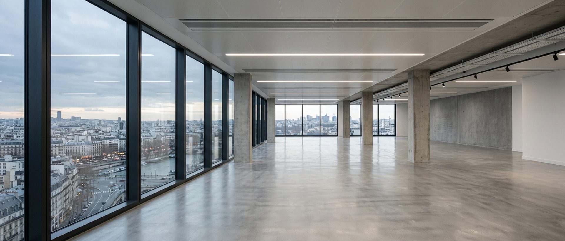 Plateau de bureaux vide aux grandes baies vitrées, sol béton ciré, lumière naturelle rasante